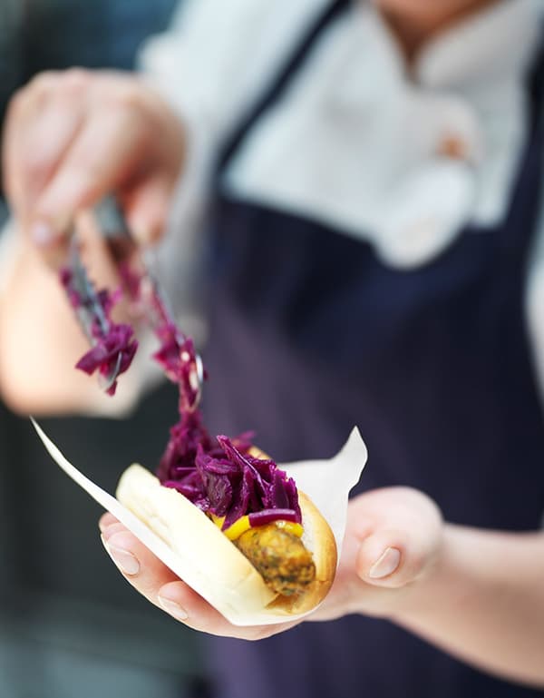 A close-up of a plant-based IKEA veggie hot dog served with bread, mustard and red cabbage.
