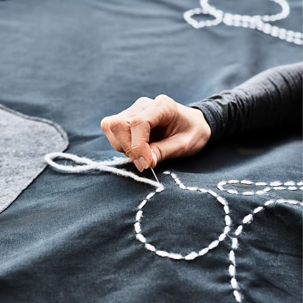 A close up of a plate outline being sewn onto a table cloth and an animated gif showing an outdoor table being covered in a table cloth that looks like a play mat with roads
