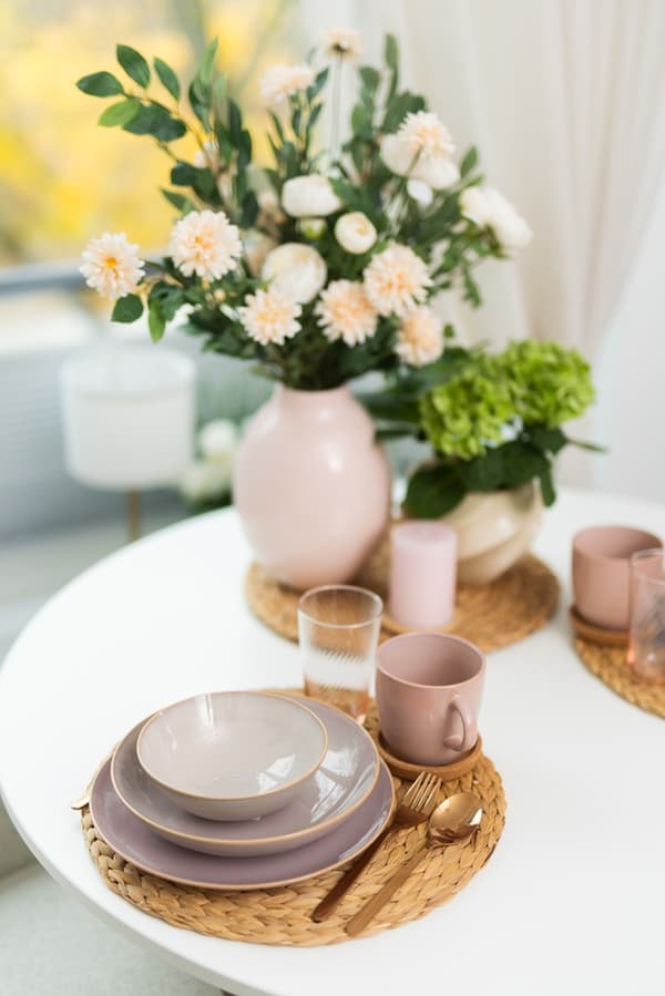 A close-up of a table setting with plates, mugs, and flowers in pastel tones.