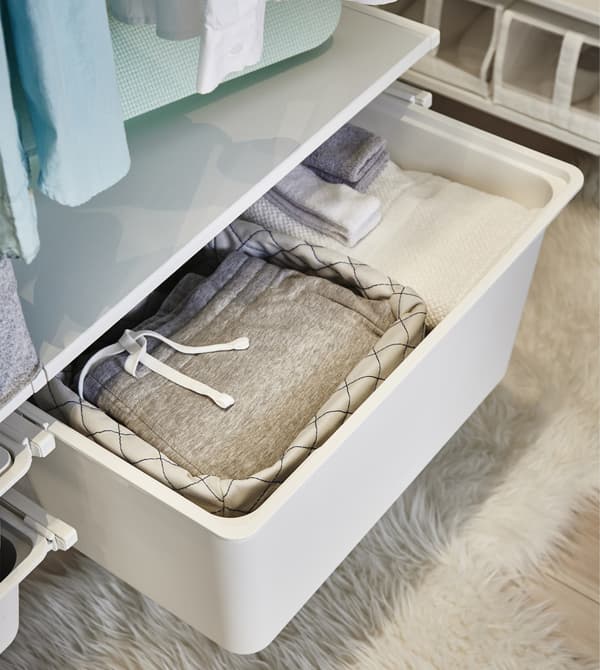 A close-up of a white ALGOT pull-out box made of plastic shown with folded sweat pants in a fabric basket.