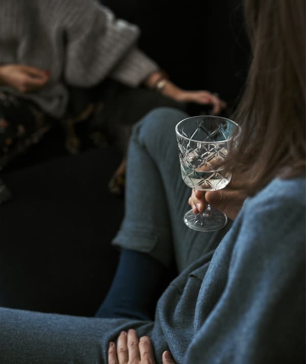 A close-up of a woman holding a drink sitting on a blue sofa.