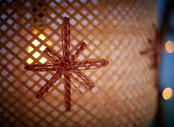 A close-up of a woven bamboo lamp decorated with paper holiday ribbon and hanging in a window.