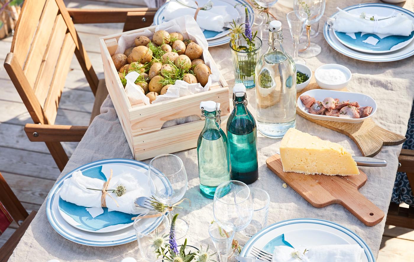 A close up of an outdoor dining table with dinnerware, glasswar, food and drink.