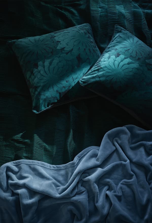 A close-up of dark green and blue bedding and cushions.