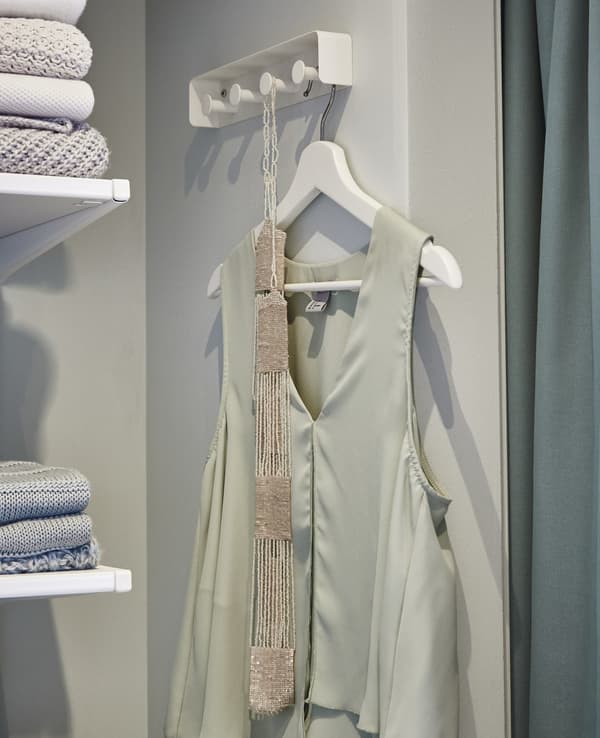 A close-up of ENUDDEN white towel rack here used as a storage place for tomorrow’s outfit, a light green top with a belt.