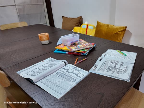 A close-up of homework, pens and candle placed on a STRANDTORP extendable dining table, for a refreshed 3-room HDB flat in Singapore, designed by IKEA home design service