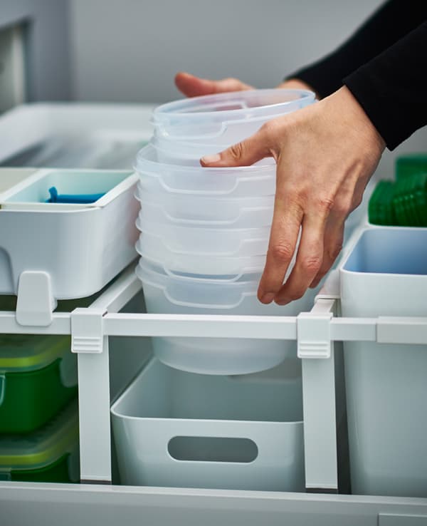 A close-up of someone putting plastic storage bins into a drawer organised with larger boxes and dividers. 