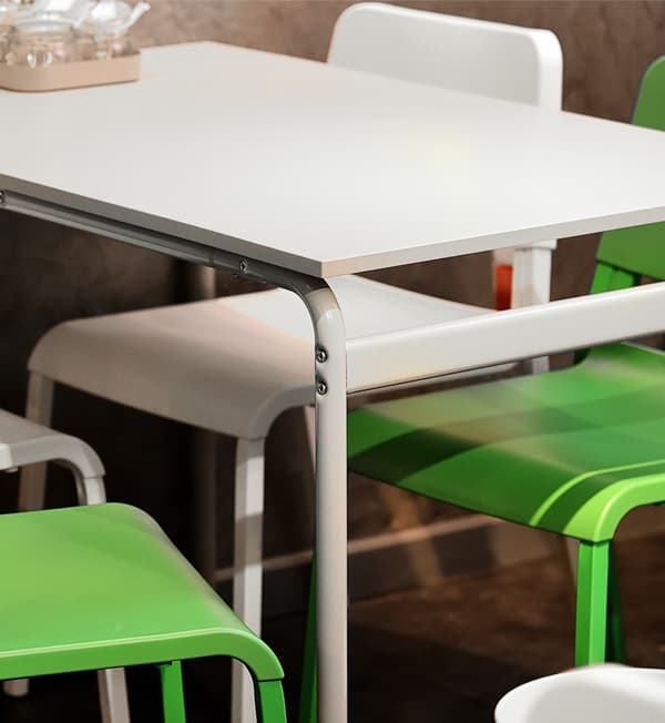 A close-up shot featuring a white table, two white chairs and green chairs.