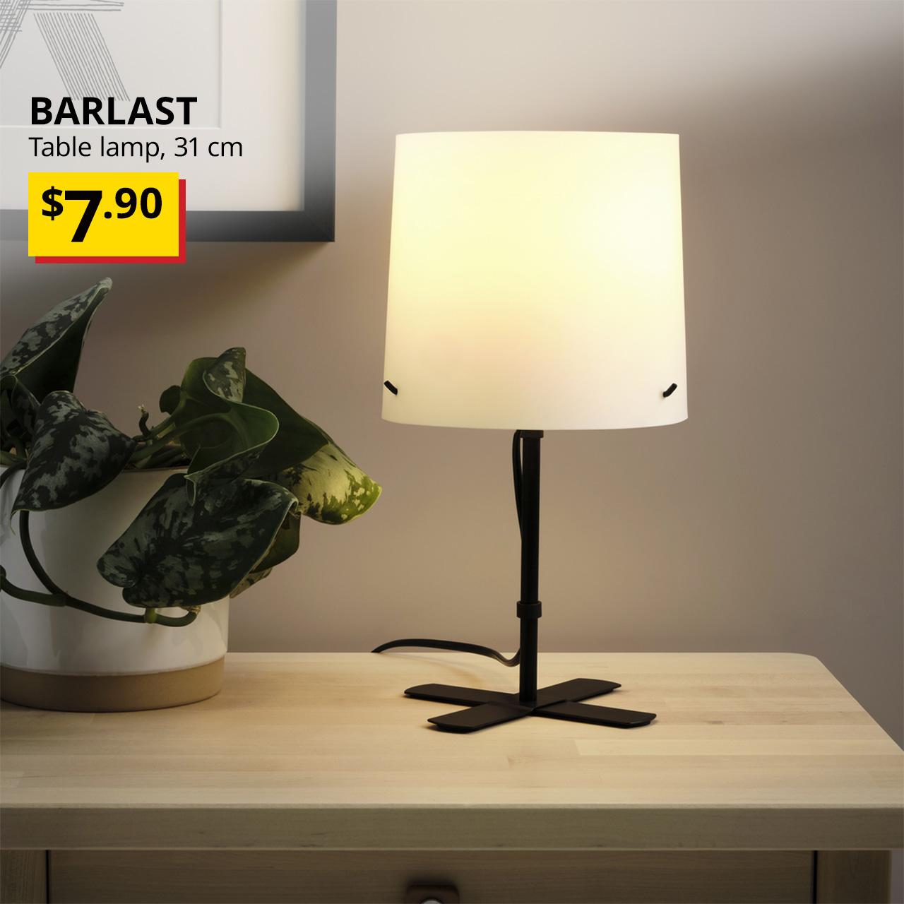 A close-up shot of a BARLAST table lamp on a sideboard. On the top left corner, black text overlay image that reads "BARLAST, Table lamp, 31 cm", with breath-taking price tag in yellow/red and text in black that states "$7.90".