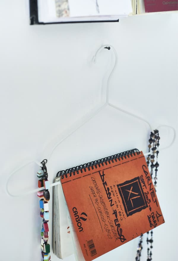 A closeup of a notebook and jewellery being displayed on a slim white clothes hanger.