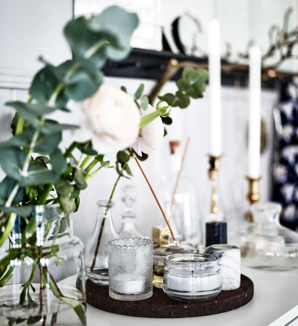 A closeup of a scent station with candles, flowers and perfumes set on circular trays or clear glass vases.