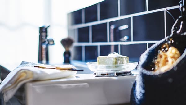 A closeup of a white sink, featuring soap in a bowl and a razor on a towel.