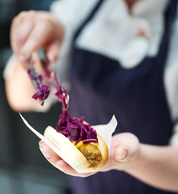 A closeup of an IKEA Bistro coworker putting red cabbage on top of a new IKEA veggie hot dog, made of plant-based foods.