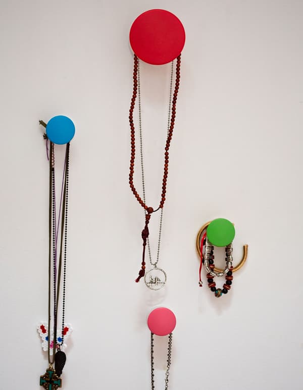 A closeup of colorful IKEA circlular chooks mounted to a white wall, hanging a collection of necklaces and bracelets.