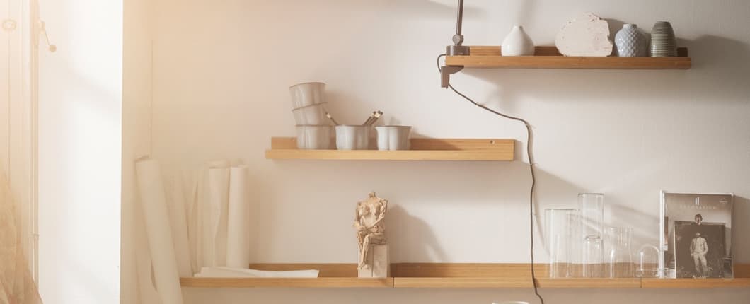 A closeup of four shelves on a wall with decorations, a light and art supplies on the shelves.