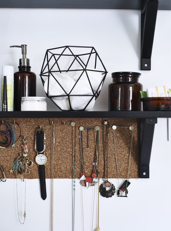 A closeup of jewellery hanging from a cork board below a black shelf.
