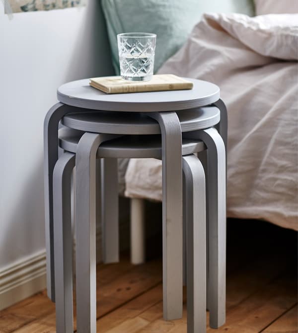 A closeup of three stacked grey stools being used as a bedside table.