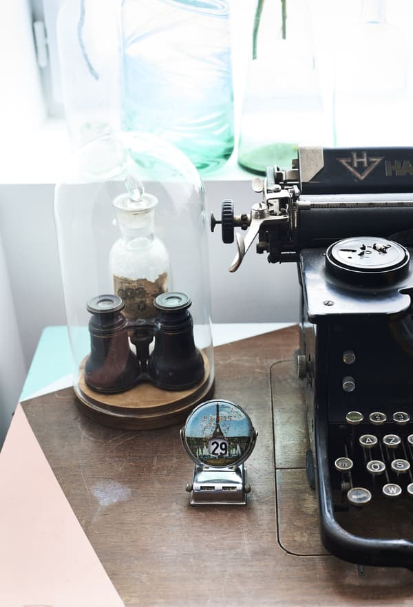 A closeup of tiny binoculars kept safely in an oval-shaped glass display case, next to a vintage typewriter.