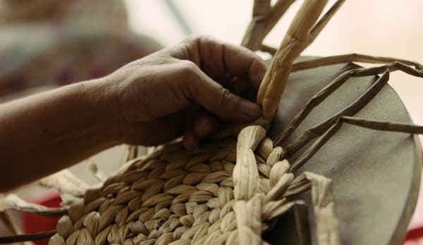 A closeup showing how aristan women expertly hand-weave an IKEA SOARÉ round place mat on a rounded surface.