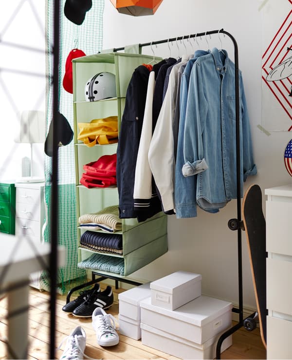 A clothes rack holds shirts on hangers and a hanging organizer. Underneath are a few boxes for shoes.