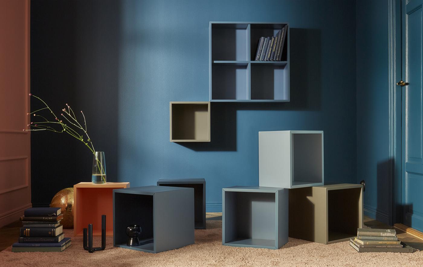 A collection of EKET open cabinets mounted to a dark blue wall and strewn across the floor in blue, brown, and grey colours.