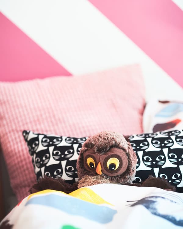 A collection of soft IKEA pink cushions and cat-patterned pillow arranged on a bunk bed, including a soft owl toy.