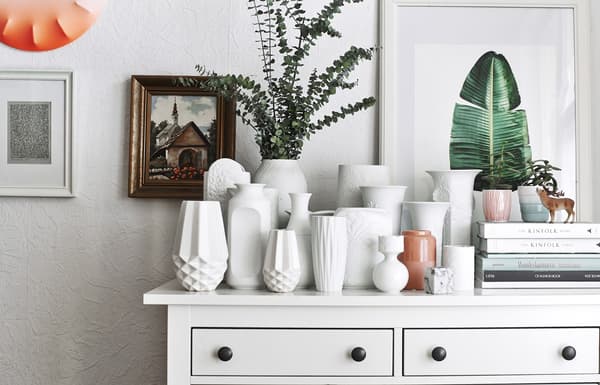 A collection of white vases on a chest of drawers.