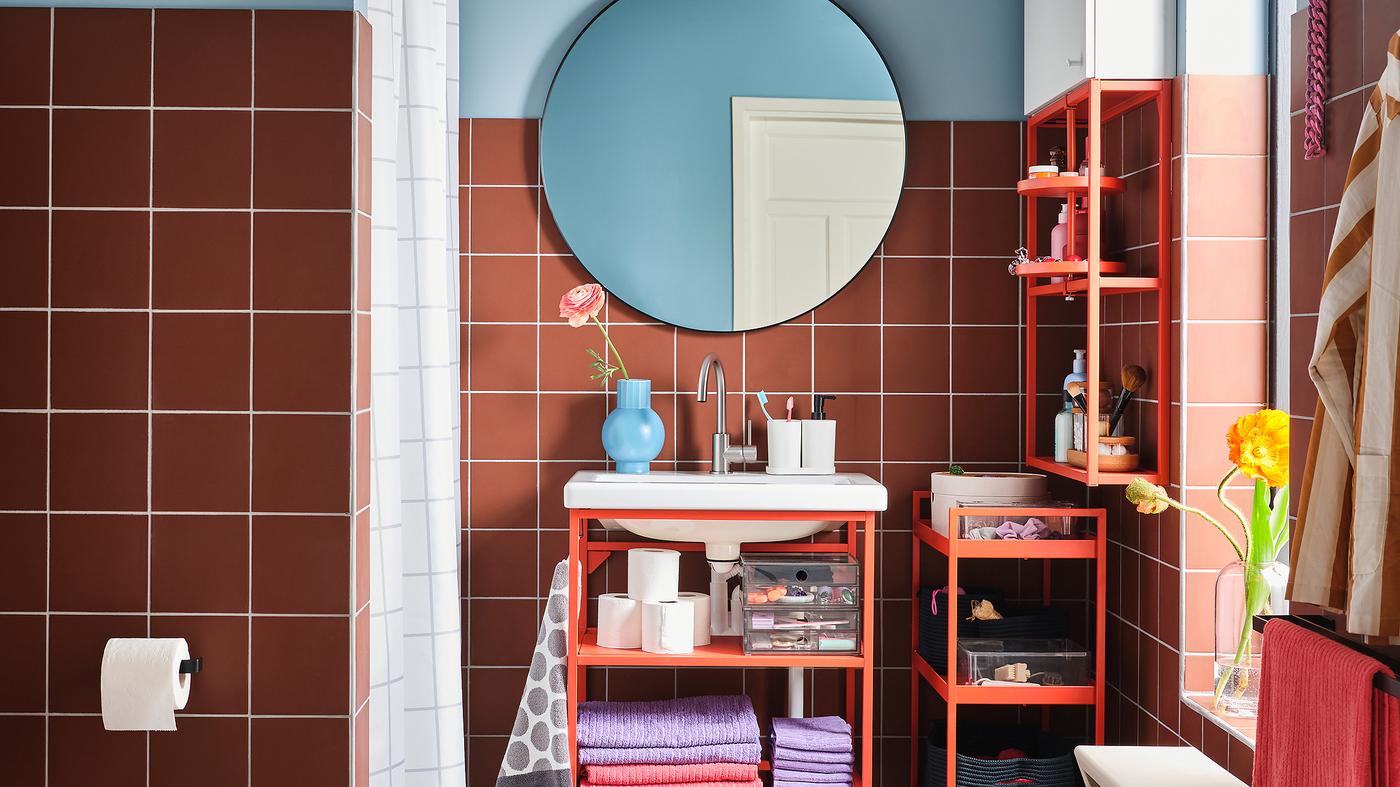 A colorful bathroom with a wash-basin unit, shelf and trolley in red-orange steel and a round mirror.