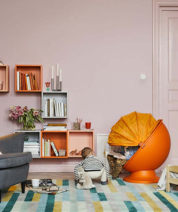 A colourful living room with a kids’ orange egg chair and two children reading and playing.