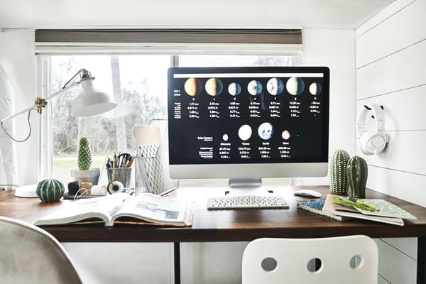 A computer monitor on a desk with notepads, files and a lamp.