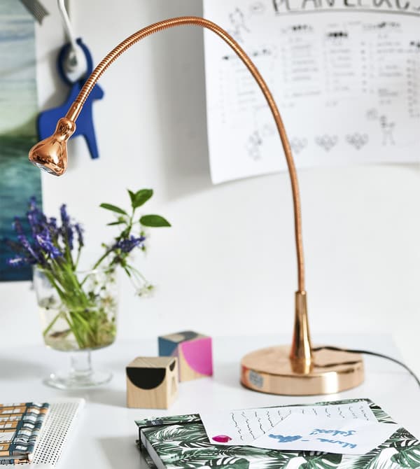 A copper lamp, flowers and stationery on a desk.