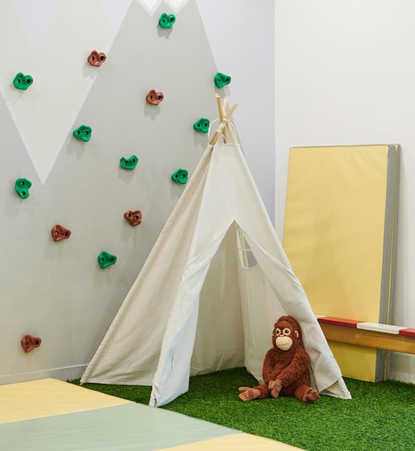 A corner featuring a child's tent placed on top of artificial grass and against a rock climbing wall.
