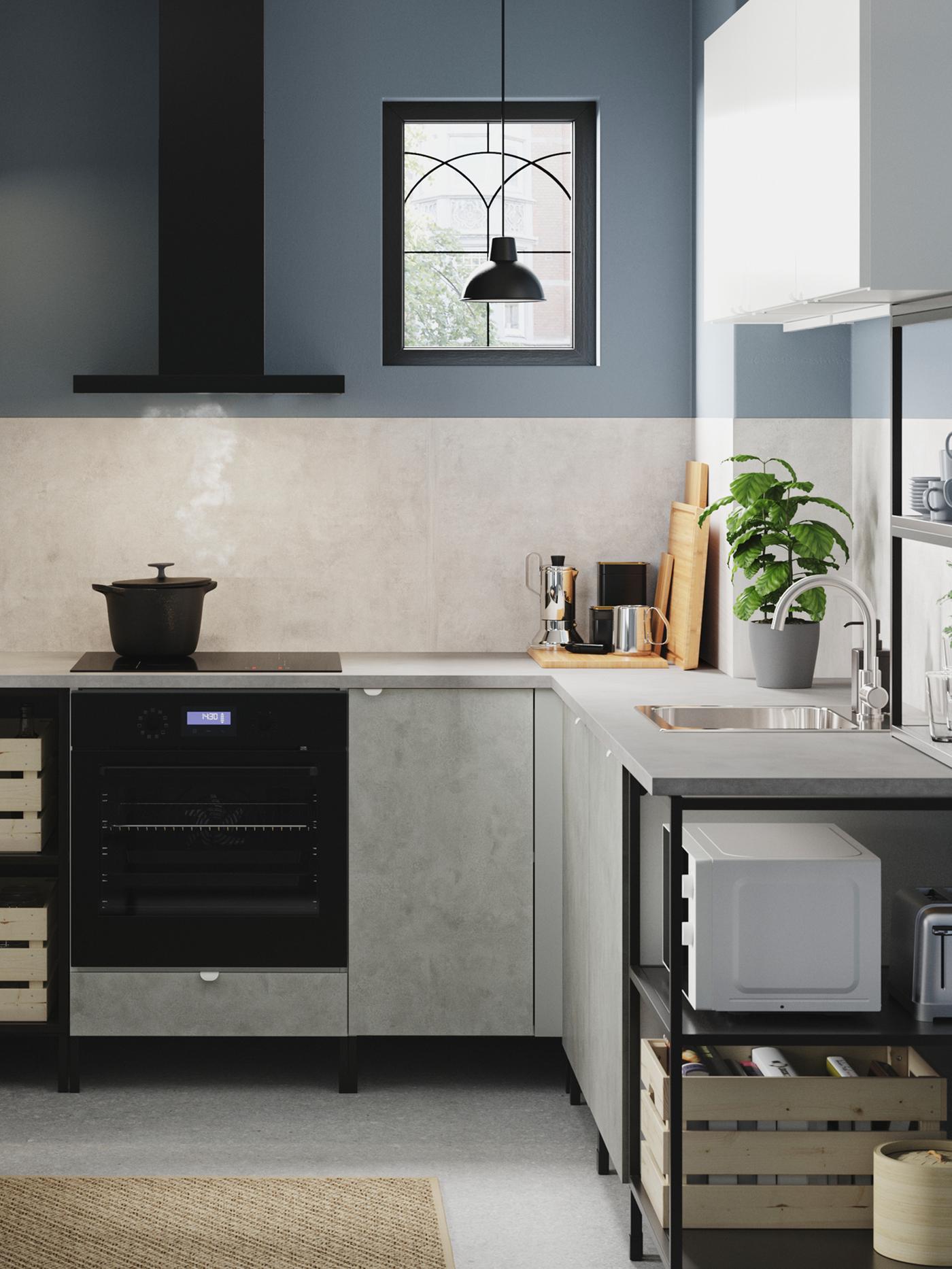 A corner kitchen in anthracite/concrete effect/white with open and closed storage, a black lamp, a plant pot and a jute rug.