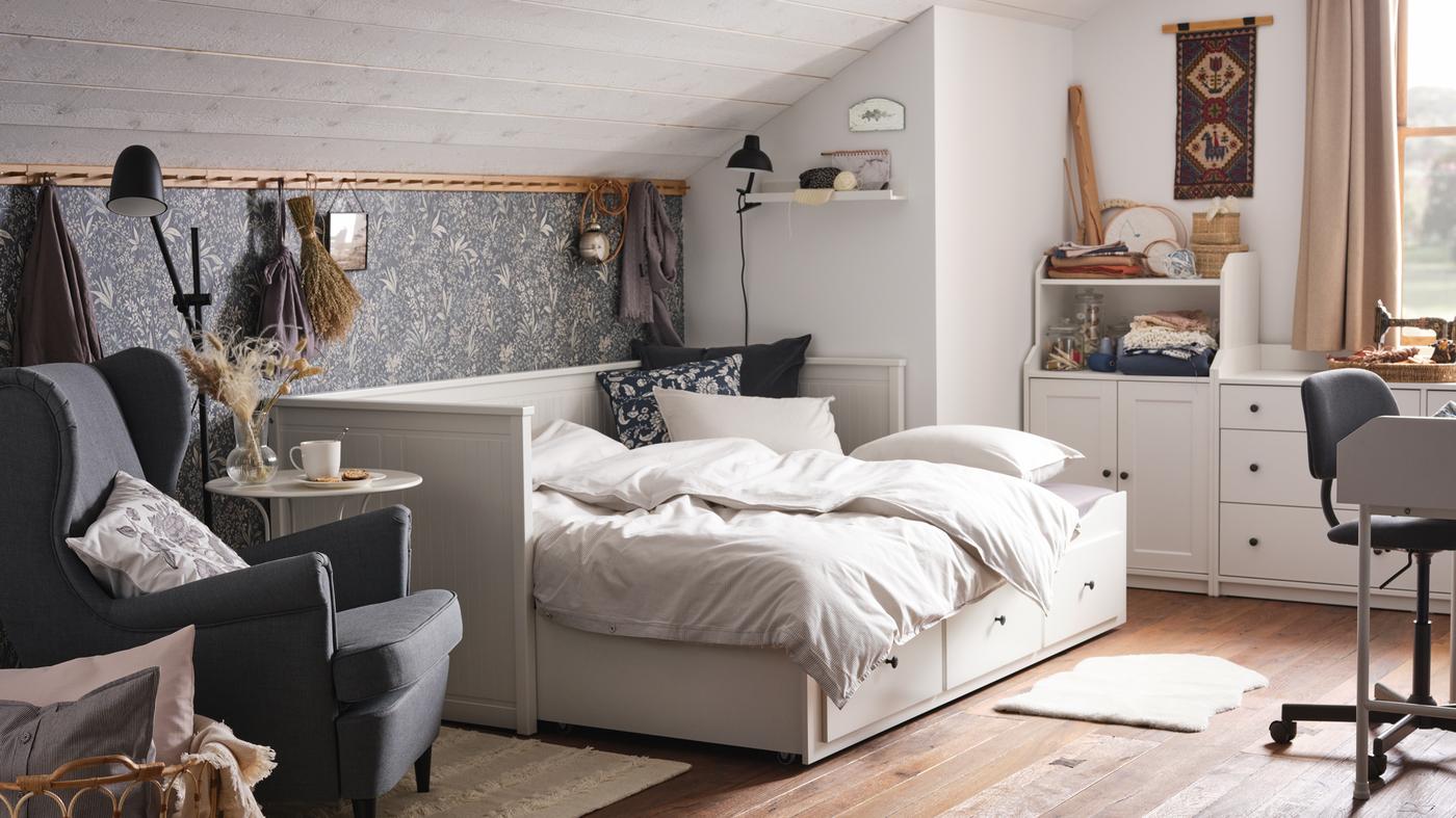 A cosy bedroom with a slanted roof, white daybed with three drawers, and white storage combination.