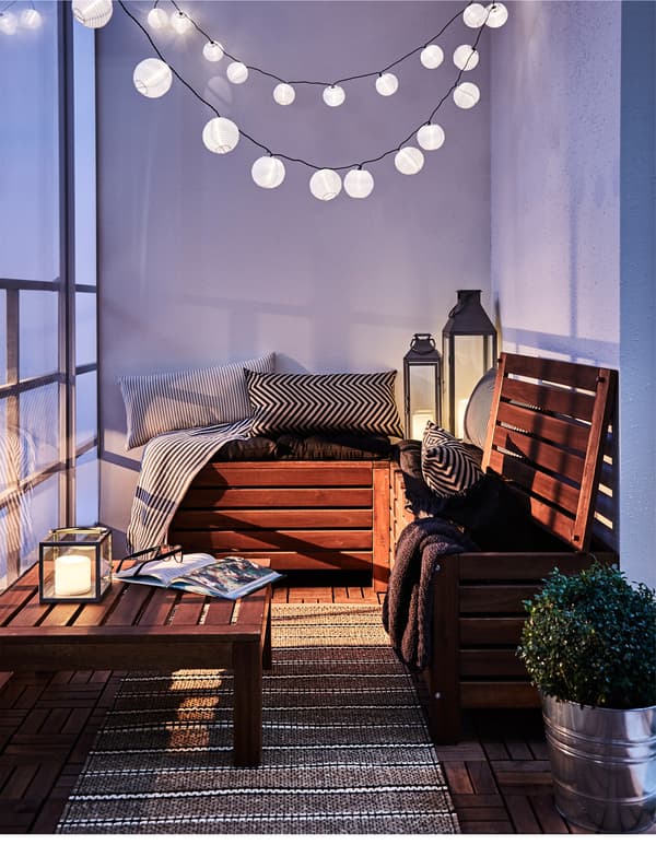A cosy corner is set up on a balcony, complete with textiles and a light chain.