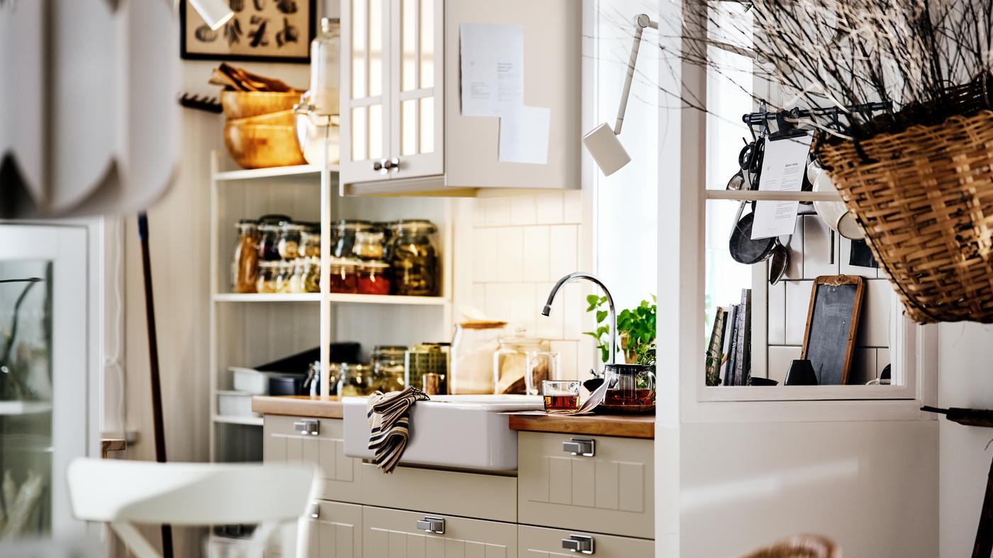 A country-style kitchen with STENSUND fronts on METOD cabinets, with a white HAVSEN sink and shelving holding jars.