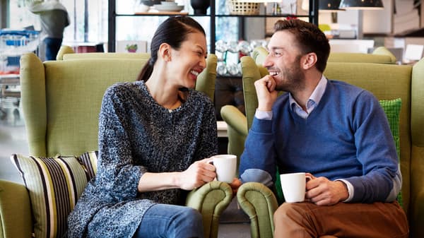 A couple sitting on comfy chair drinking coffee and laughing