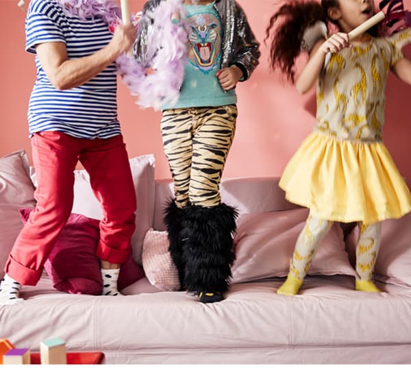 A cropped image showing three young children's legs on top of a pink sofa as they play together.