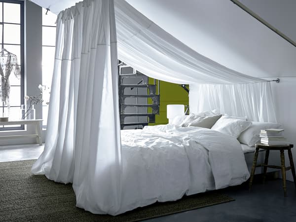A curtain wire is fastened to the wall and a sloped ceiling, over the white bright bed hangs a dreamy textile.