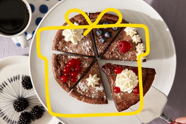 A cut up chocolate cake on a white plate, with berries and cream.