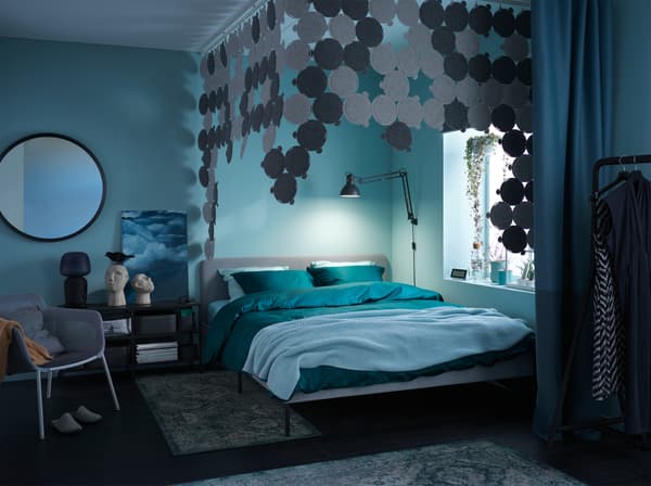 A dark and cosy bedroom filled with green and blue textiles, sound absorbing panels, and comfortable rugs.