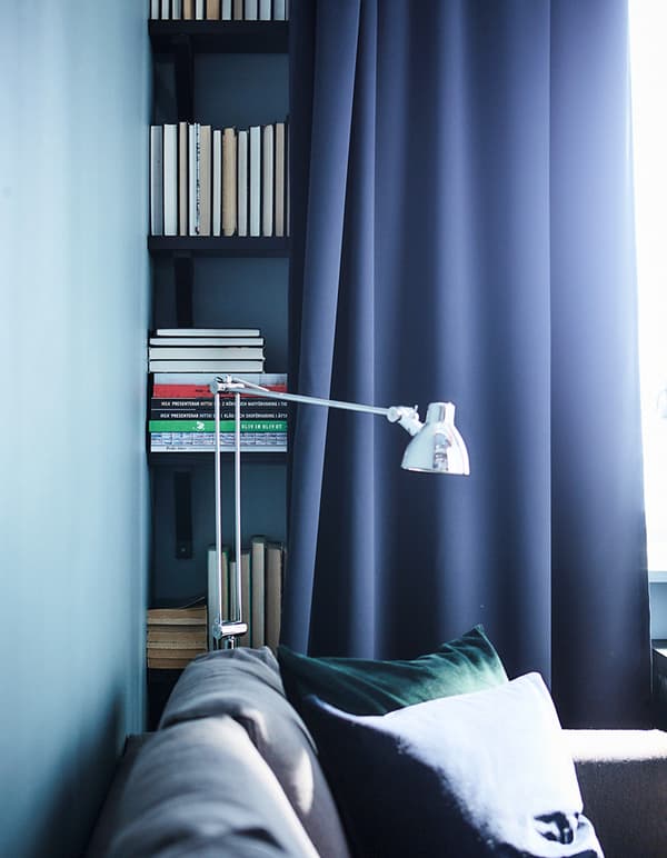 A dark blue curtain in front of a bookshelf, in a living room setting, used to hide the storage solution.