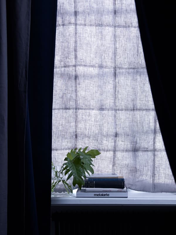 A dark-blue soundproofed curtain hanging in a window, over a table with books, and blocks out outdoor noise and daylight.