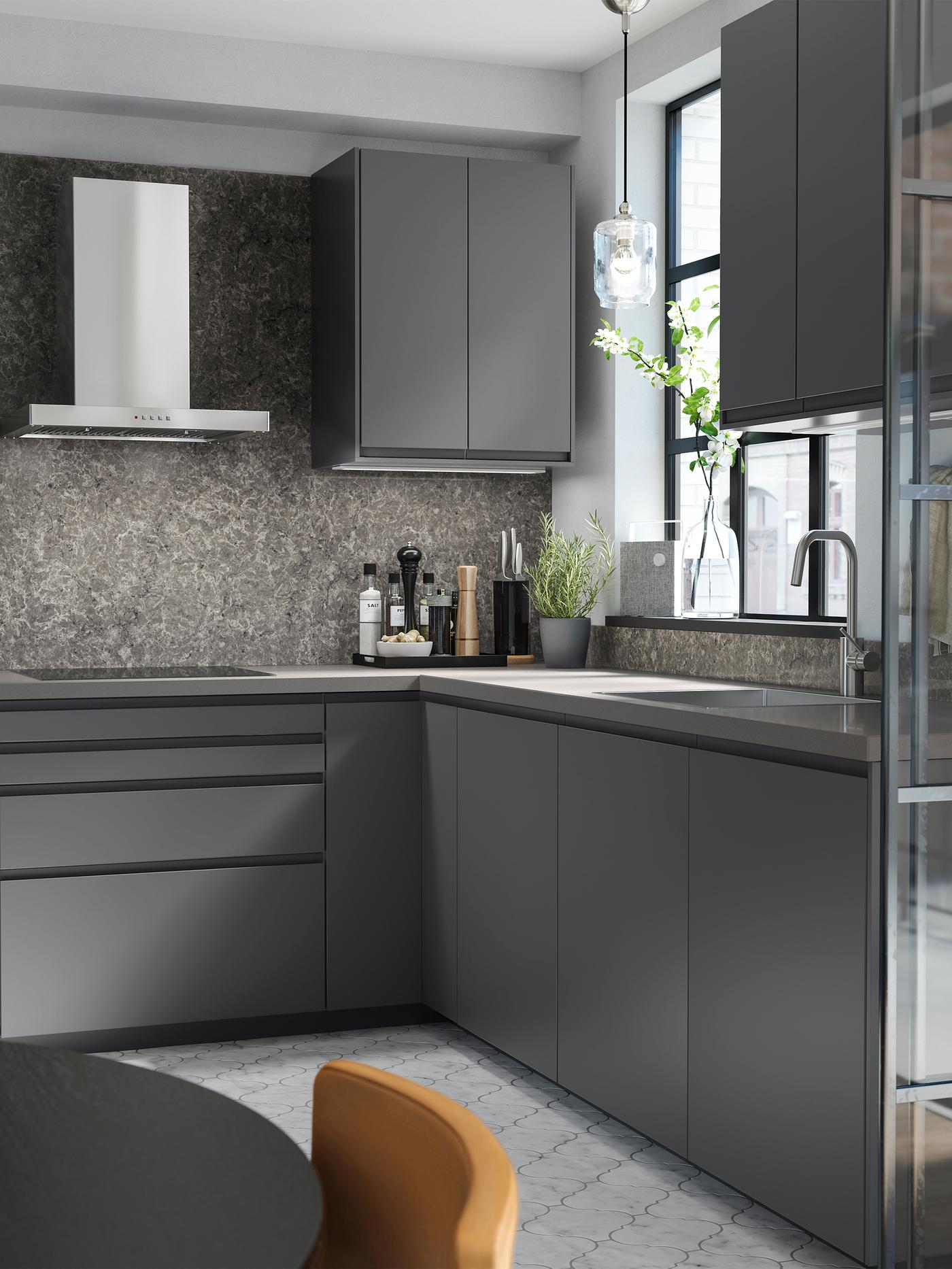 A dark-grey kitchen with dark-grey cabinets, a wall mounted extractor hood in stainless steel colour and a patterned floor.