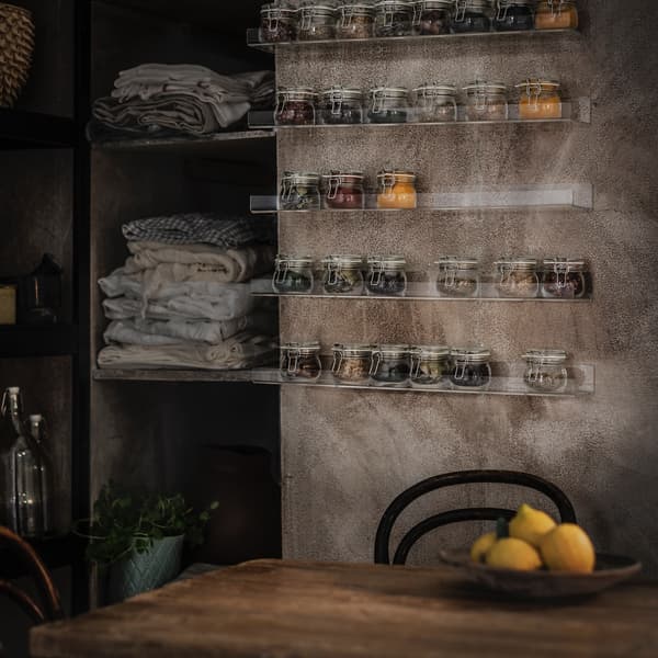 A dark kitchen space with clear wall shelves holding spice jars.