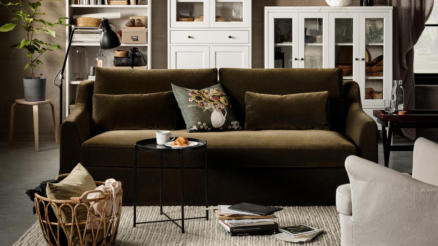 A dark olive-green 2-seat sofa, a white high cabinet with glass doors and 1 drawer, a white bookcase, a birch stool.