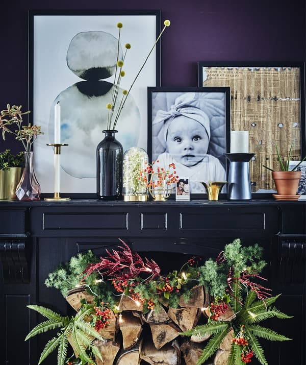 A dark painted fireplace with festive decoration and personal objects displayed on top.
