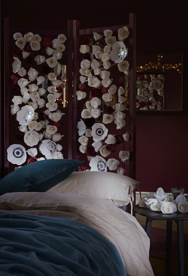A dark red bedroom with a bed dressed in blue and white bedding and a floral screen.