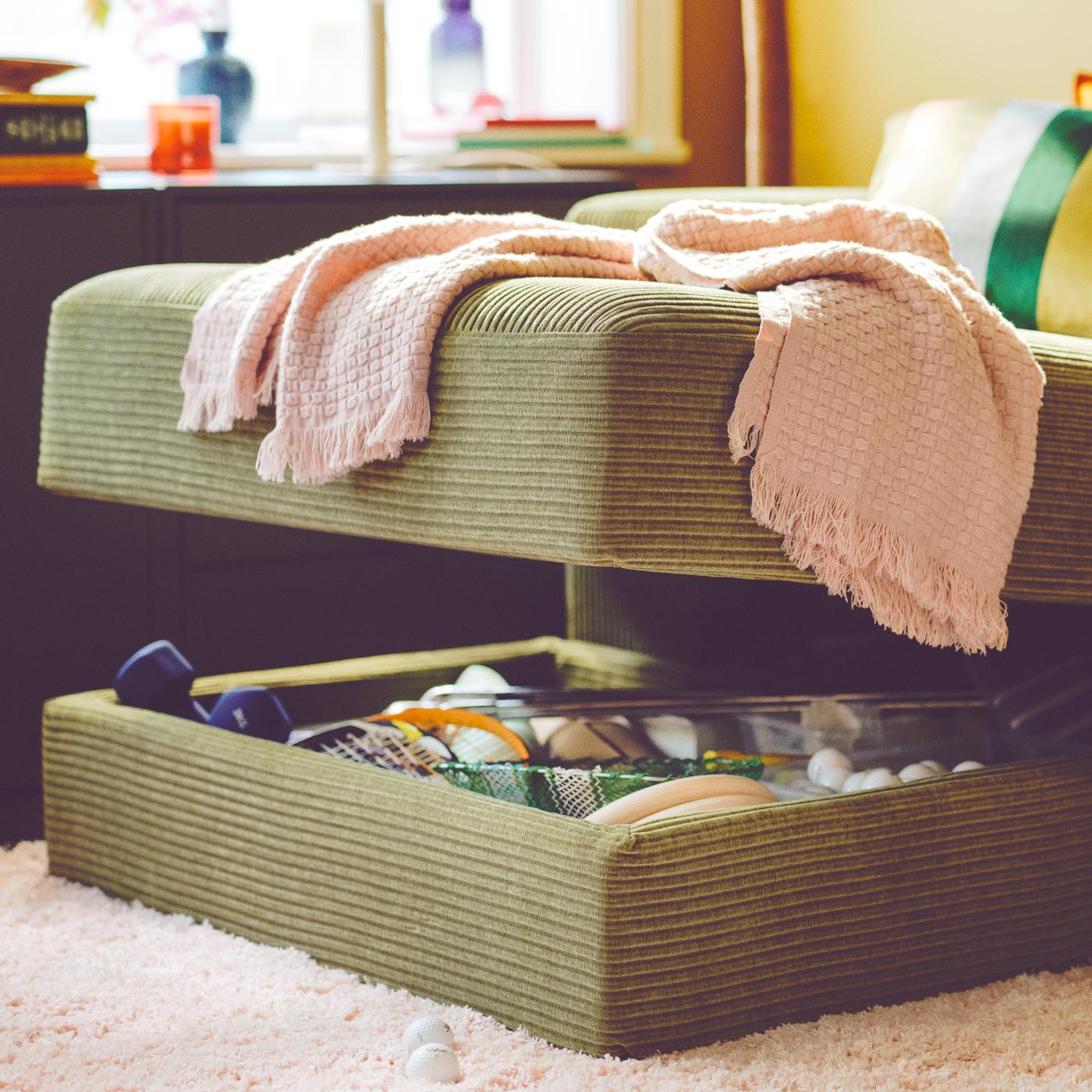 A dark yellow-green JÄTTEBO chaise longue has a hidden storage compartment opened, showing things inside.