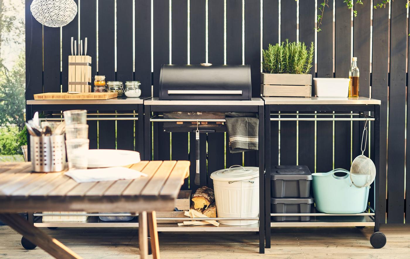 A decked area in a garden with barebque and food trolleys.